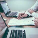 Projektmanagement als Umsatztreiber Zwei Personen sitzen vor ihren Laptops und skizzieren etwas auf ein Blatt Papier