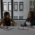 Jobsharing: Das steckt hinter dem Trend Zwei Frauen sitzen an einem Tisch einander zugewandt und reden miteinander. Vor ihnen liegen Notizhefte