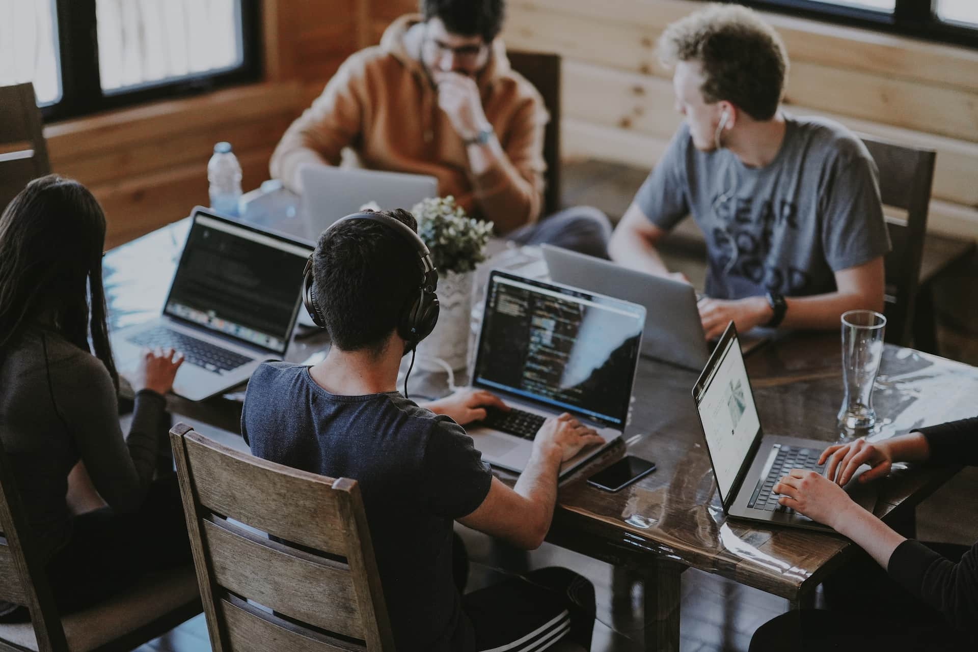 Auf dem Foto sitzen fünf Menschen an einem Schreibtisch, alle haben einen Laptop vor sich und arbeiten