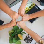 Teamwork in factro täglich leben Fünf Personen stehen im Kreis und stecken ihre Faust in die Mitte.