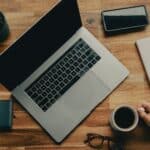 Remote Leadership: Führung auf Distanz meistern Ein Laptop steht auf dem Schreibtisch, ein Handy und ein Notizblock.