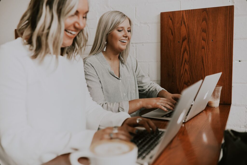 Zwei Frauen sitzen nebeneinander an einem Tisch und arbeiten am Laptop