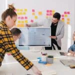 Agile Verwaltung: Methoden und Herausforderungen Mehrere Menschen abreiten zusammen an einem Tisch, auf dem Zettel verteilt liegen