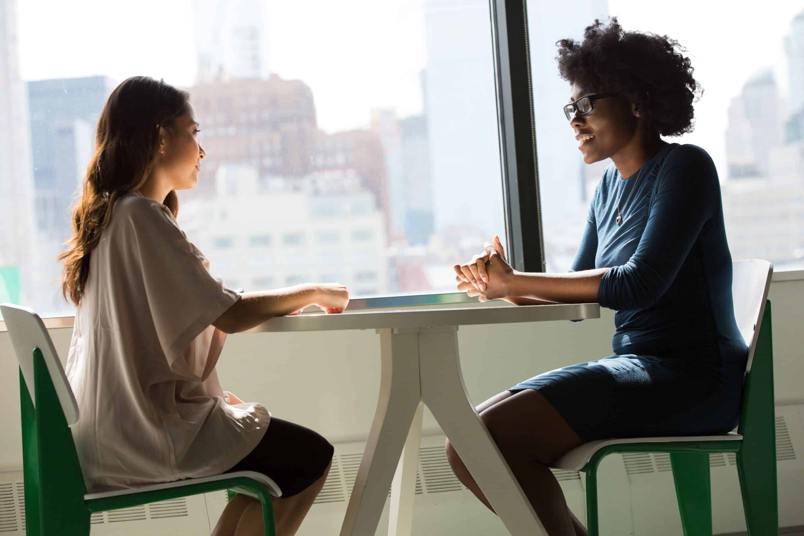Zwei Frauen sitzen sich an einem Tisch gegenüber und reden