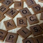 Kleine flache Holzquadrate mit aufgedruckte Buchstaben liegen verteilt auf einem Tisch