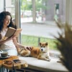Work-Life-Blending: Flexibles Arbeiten neu gedacht Eine Frau sitzt neben ihrem Hund am Fenster und liest