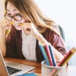 Scope Creep im Projektmanagement erkennen: Ursachen & Tipps Eine Frau sitzt vor einem Laptop und beißt frustriert auf einen Stift