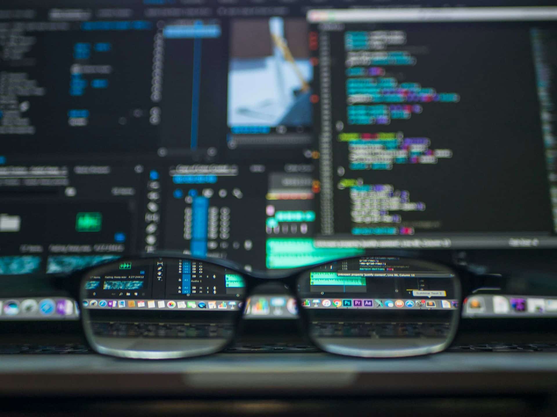 Eine Brille liegt vor einem Computerbildschirm. In den Brillengläser sieht man Icons auf dem Display, alles außen herum ist verschwommen